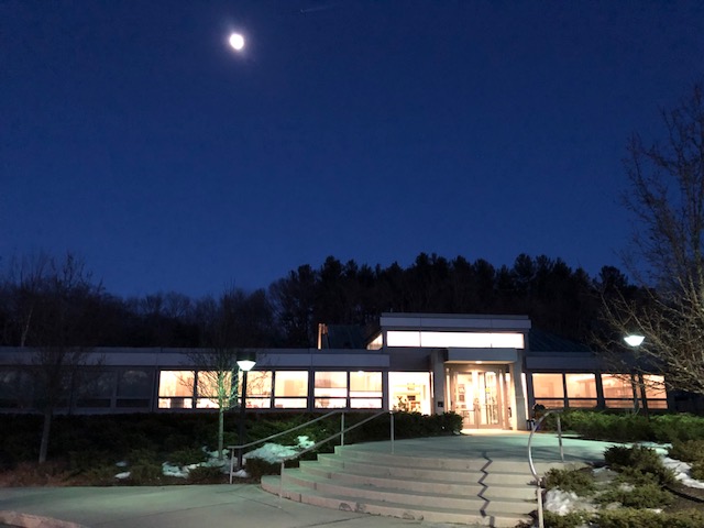 Synagogue building illuminated at night with moon in the sky and entrance steps leading inside